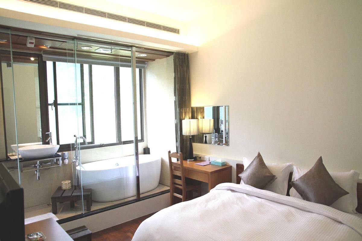 Une chambre d’hôtel avec un grand lit, un bureau, une chaise, une salle de bain avec un lavabo et une baignoire, et un grand miroir.