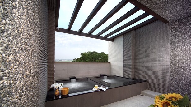 A modern spa area with a large hot tub, a wooden bench, and a view of the landscape. - Peace Area Hot Spring Hotel (Jiaoxi)
