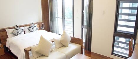 Una habitación de hotel moderna con una cama grande, un sofá, una mesita y vistas de la ciudad a través de amplias ventanas.