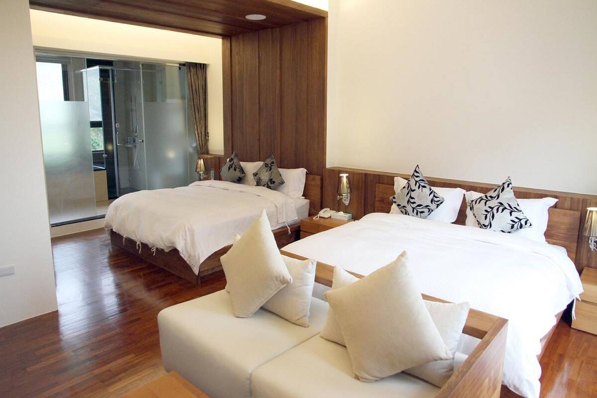 Une chambre d’hôtel avec deux lits, un canapé et une porte vitrée donnant sur un balcon.