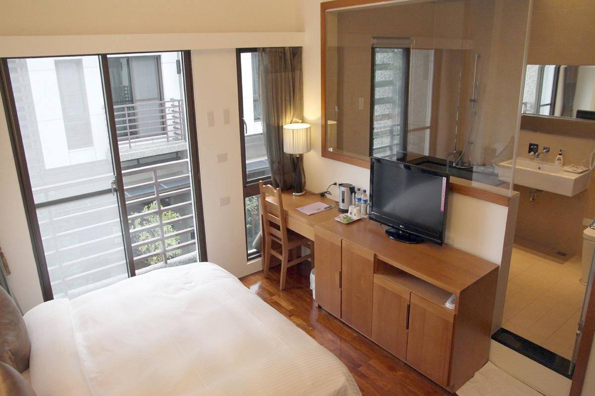 Une chambre d’hôtel comprenant un lit, un bureau avec une télévision, un miroir et une salle de bain avec un lavabo et des toilettes.