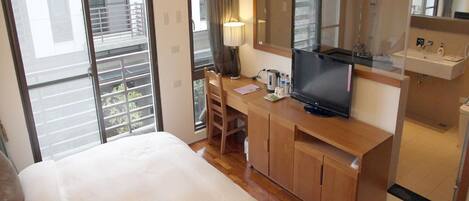 A hotel room with a bed, a desk with a TV, a mirror, and a bathroom with a sink and toilet.