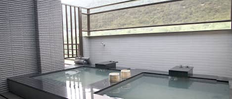 Un spa moderno con un hidromasaje cubierto de vidrio, escalones de madera y vistas a una ladera boscosa.