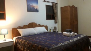 A neatly made bed with a patterned bedspread, a wooden headboard, a nightstand with a lamp, a window with curtains, and a wardrobe. - 4 Bedroom House & Private Pool Pattaya (Pattaya)