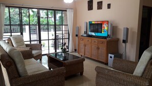 A living room with wicker furniture, a glass coffee table, a television, and a view of the outdoors through large windows. - 4 Bedroom House & Private Pool Pattaya (Pattaya)