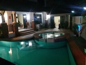 Une piscine avec un jacuzzi, entourée d’un patio avec des marches menant à un espace salon couvert.