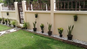 A garden with potted plants arranged along a wall, a gravel path, and a grassy area. - 4 Bedroom House & Private Pool Pattaya (Pattaya)