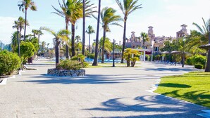 A paved pathway lined with palm trees and a stone wall, leading to a building with a tower. - Bungalows Bahia Sur (San Fernando)