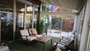 A spacious patio area with a green artificial turf, wooden furniture, and large sliding glass doors leading to an outdoor space. - Grand Nora Hotel (Ankara)