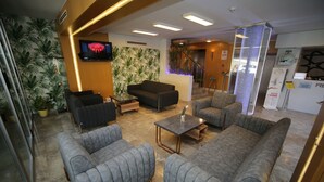 A modern lobby with grey sofas, a flat-screen TV, a staircase, and a reception desk. - Grand Nora Hotel (Ankara)