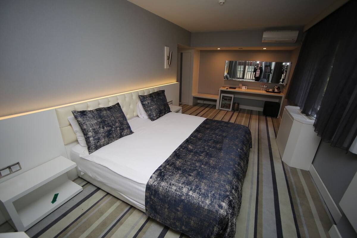 Une chambre d’hôtel moderne avec un grand lit, une table de chevet, un bureau avec une chaise et un miroir.