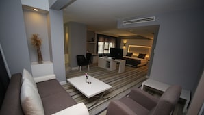 A modern living room with a sofa, armchairs, a coffee table, and a TV. - Grand Nora Hotel (Ankara)