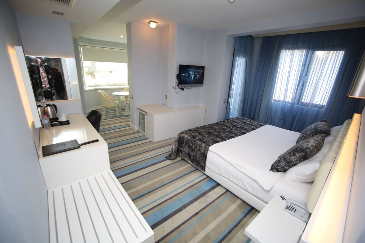 Une chambre d’hôtel équipée d’un lit, d’une table de chevet, d’un bureau, d’une chaise et d’un téléviseur fixé au mur.