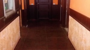 Un couloir avec un comptoir d’accueil sur la gauche, une porte en bois sombre au fond, et un sol carrelé.