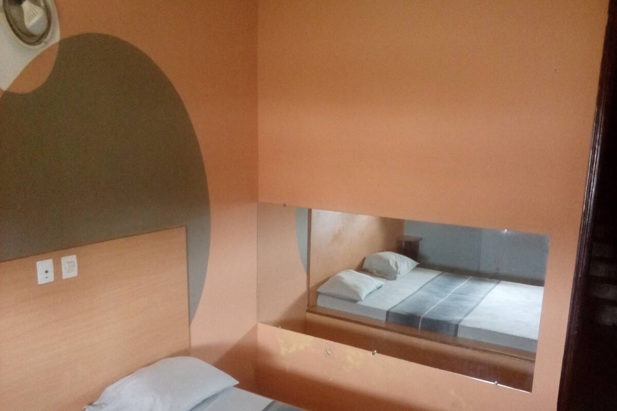 A single bed with a striped mattress, a headboard, and a mirror above it.