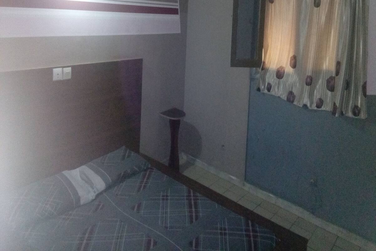 A room with a bed, a small table, a wall-mounted air conditioner, and a window with curtains.