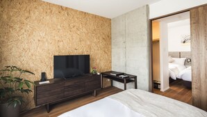 A modern bedroom with a large bed, a TV on a wooden console, a small table, and a potted plant.