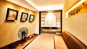 A modern interior with a sofa, framed artwork, a fan, and a window with curtains.