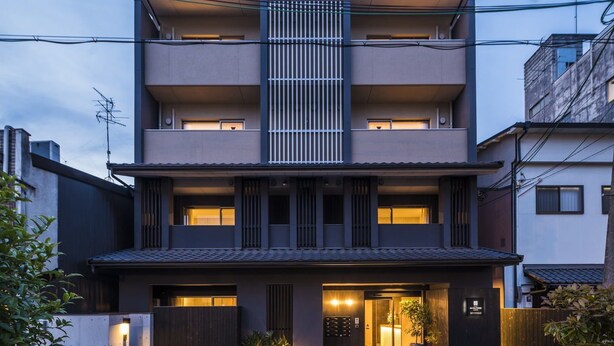 A modern two-story building with a central vertical light feature, a gated entrance, and a small garden area.