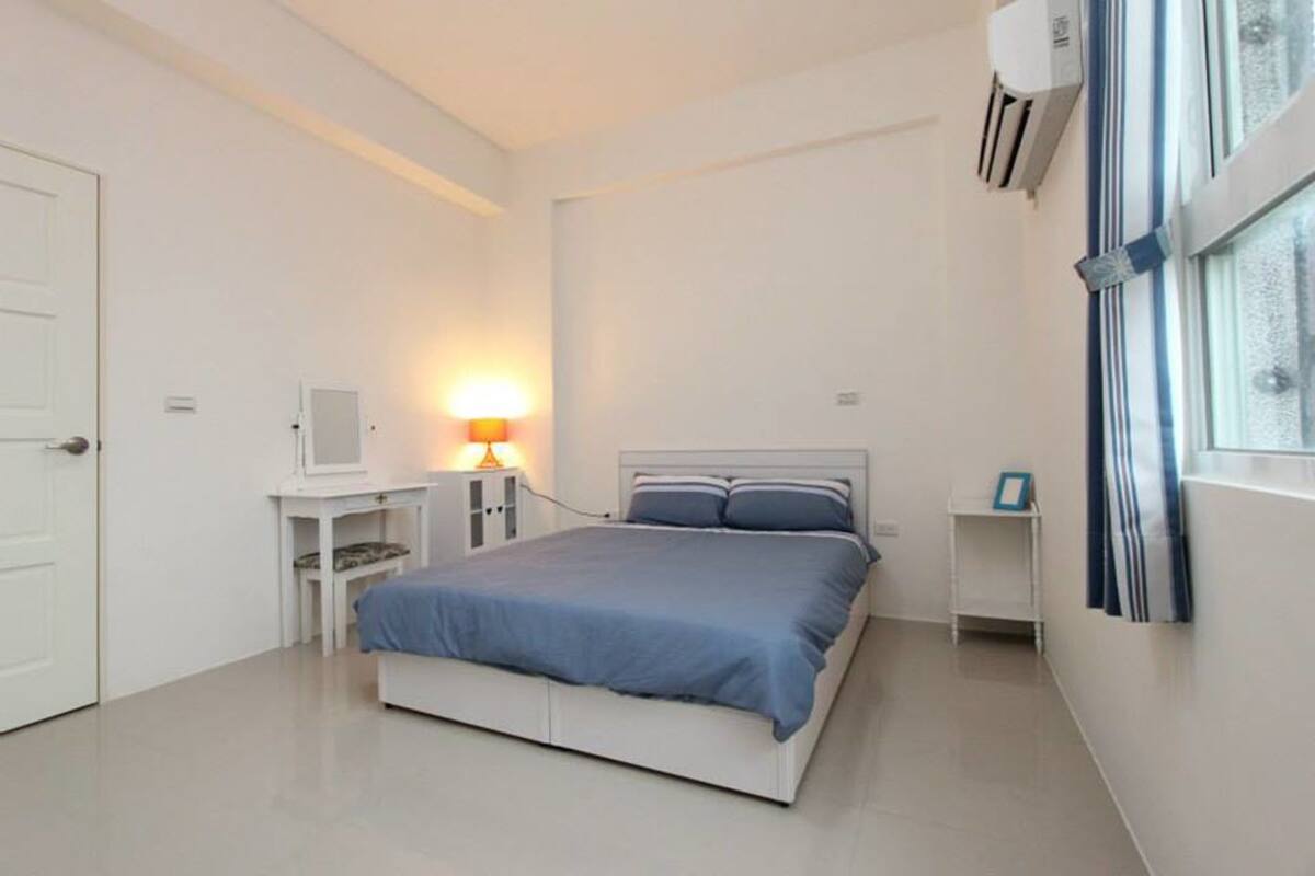 A bedroom with a bed, bedside tables, a lamp, a TV, and an air conditioning unit.