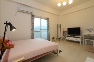 A bedroom with a bed, a TV, a desk, and a window with curtains.