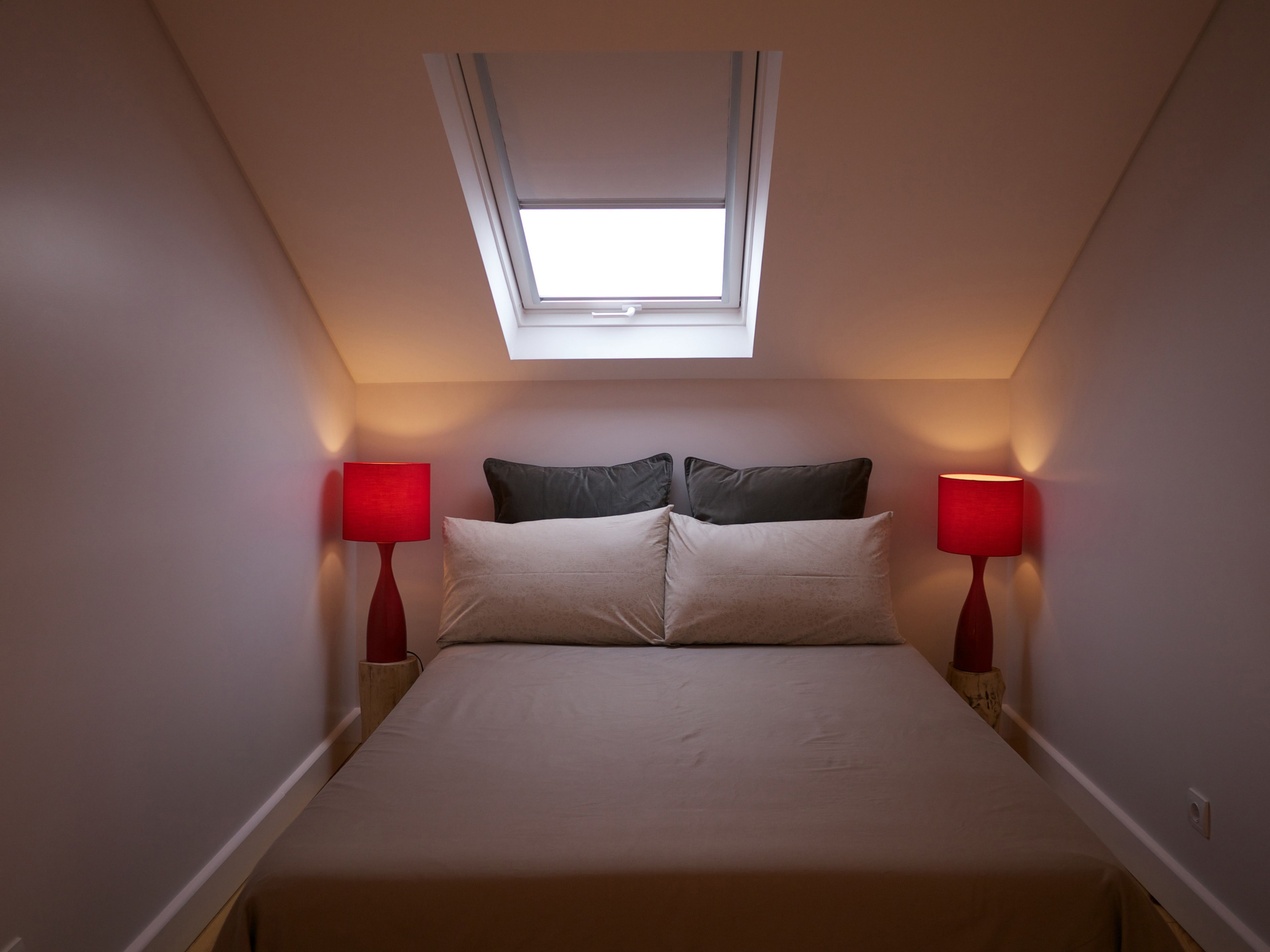 Une chambre avec un puits de lumière, un lit avec deux oreillers et deux lampes de chevet.