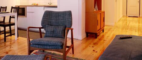 A modern living room with a wooden floor, a blue patterned armchair, a wooden cabinet, and a remote control on a cushion.