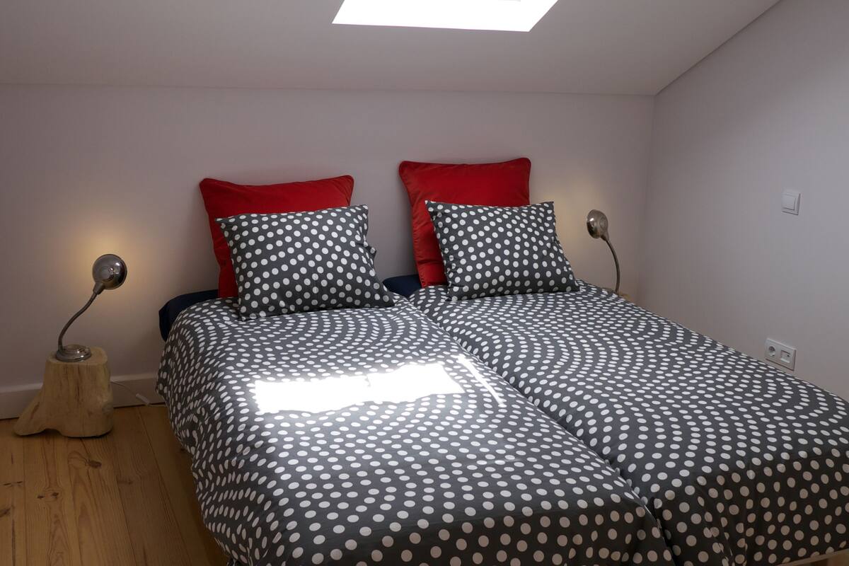 A bedroom with a skylight, a bed with polka dot bedding, red pillows, and two bedside lamps.