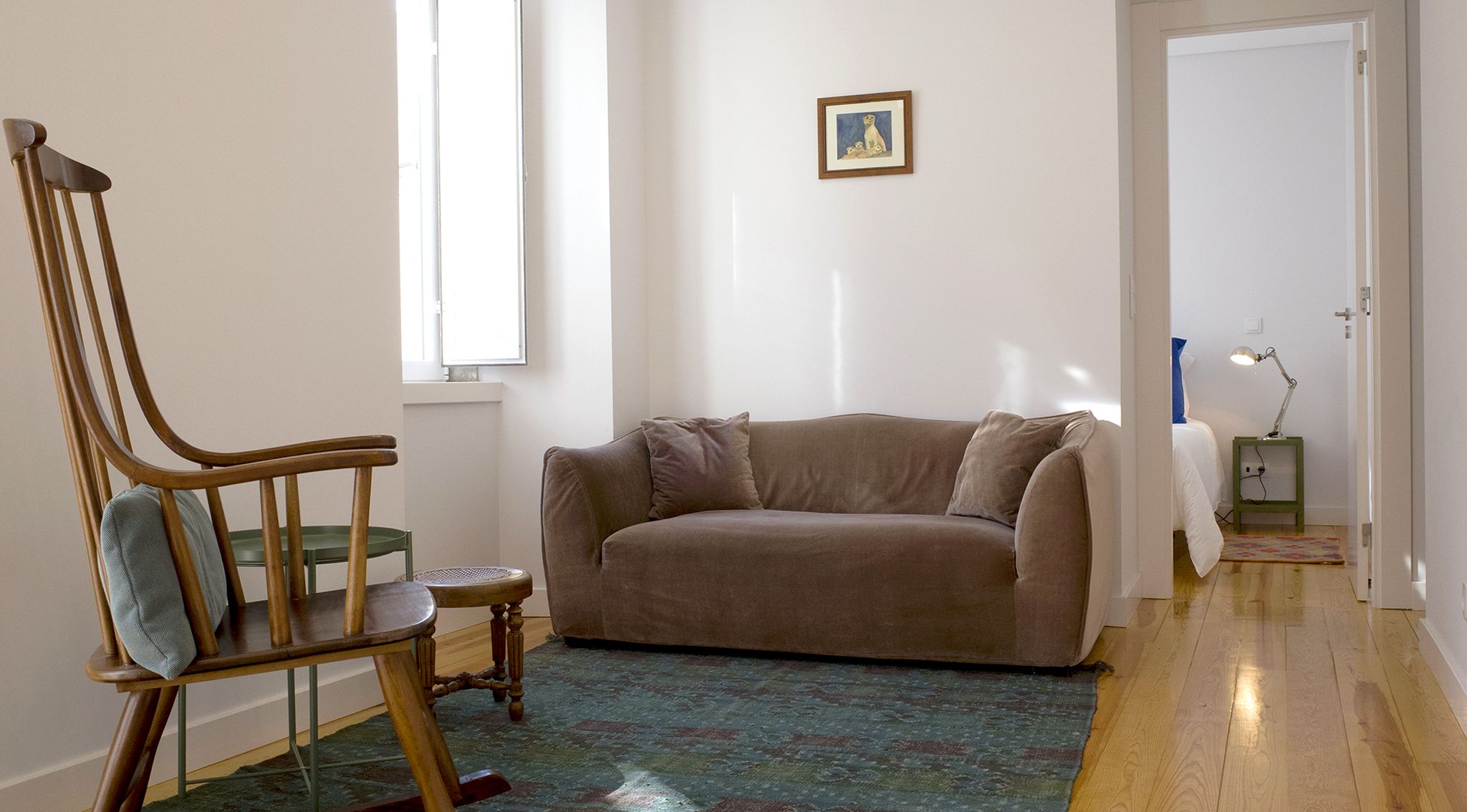 Une pièce comprenant une chaise en bois, un canapé beige, une petite table ronde et un tapis coloré.
