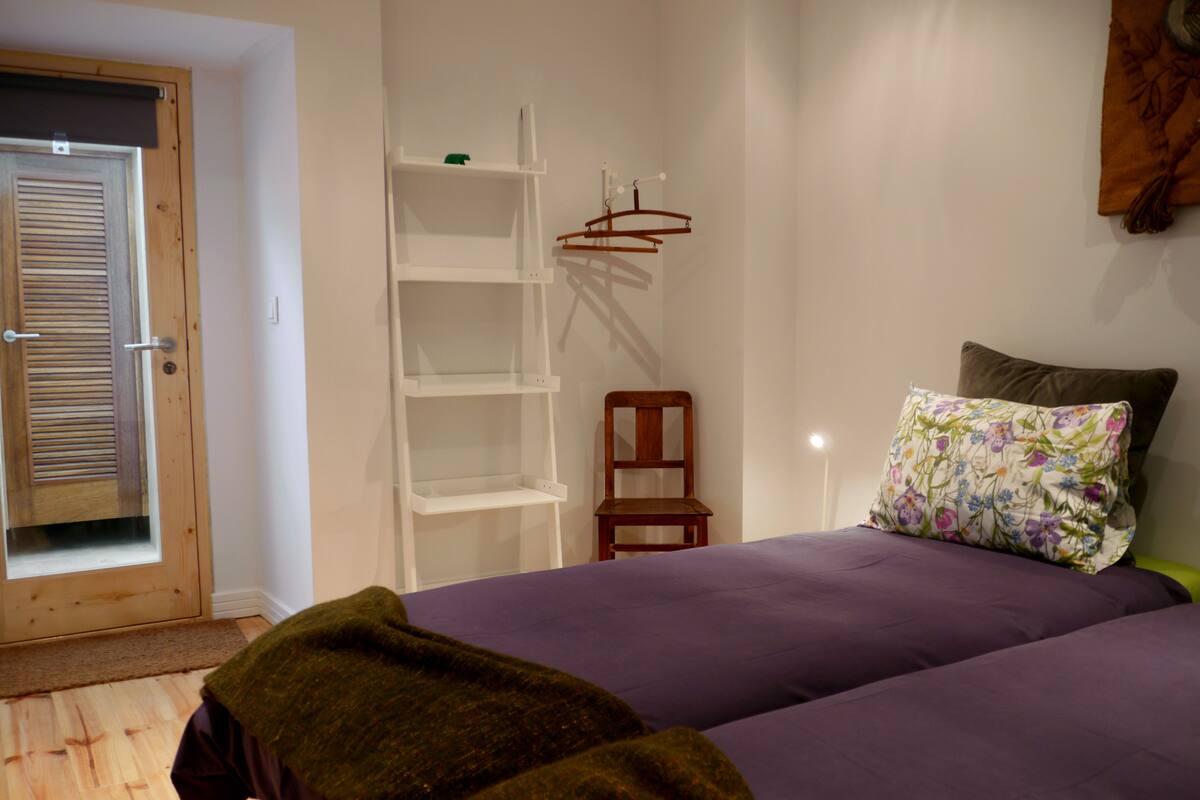 A bedroom with a bed, a chair, a shelf, and a door.