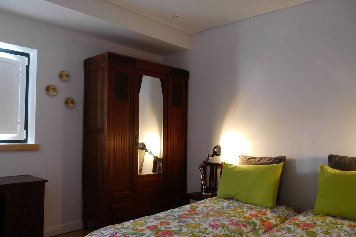 A bedroom with a bed, a wooden wardrobe, a desk, and a window.