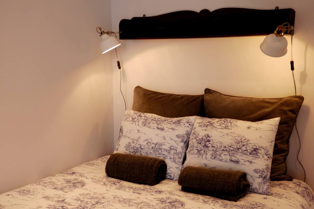 A bed with a headboard, two pillows, and two rolled-up blankets.