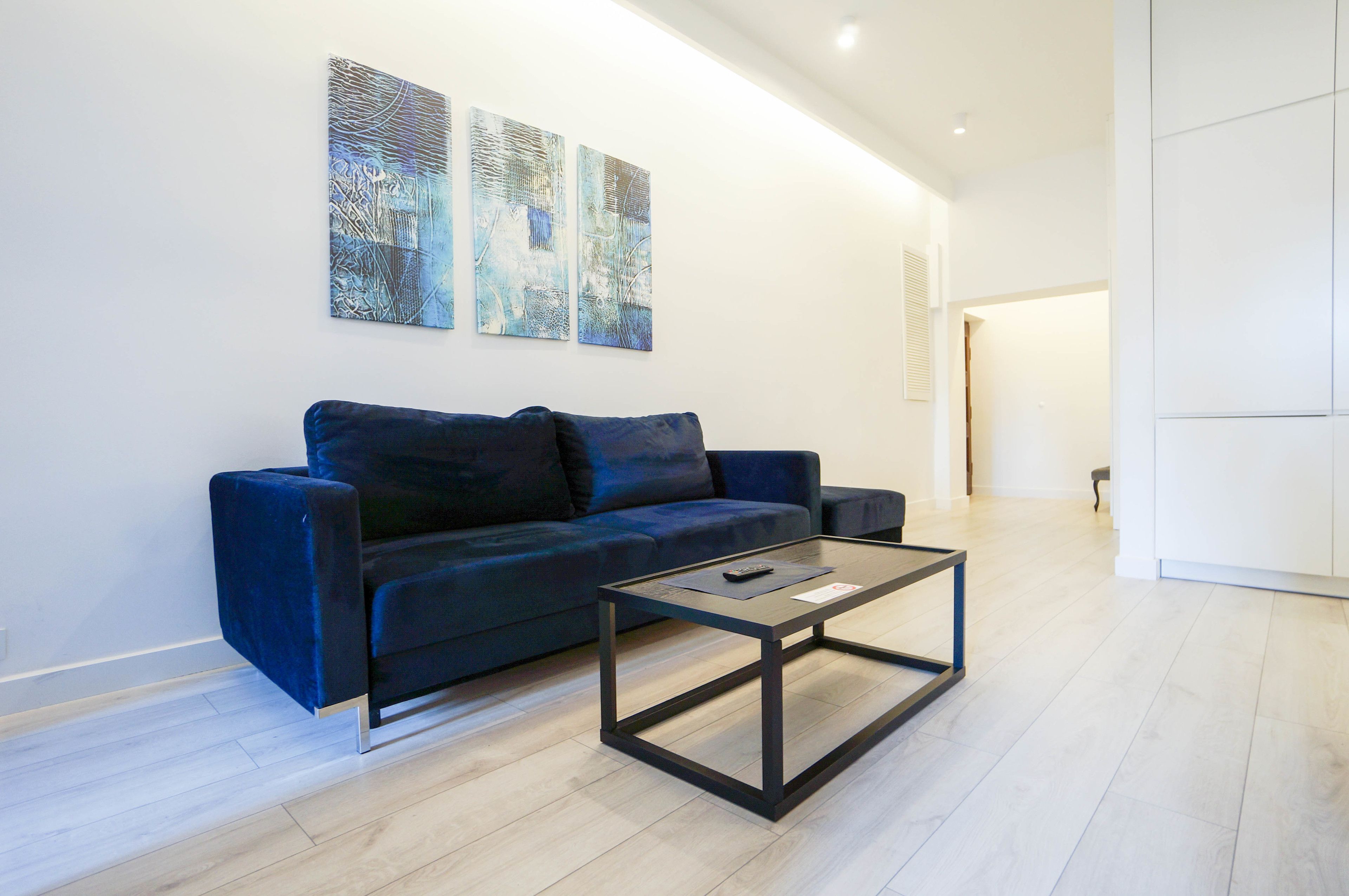 Una sala de estar moderna con un sofá azul oscuro, una mesa de centro con cubierta de vidrio y arte abstracto en la pared.