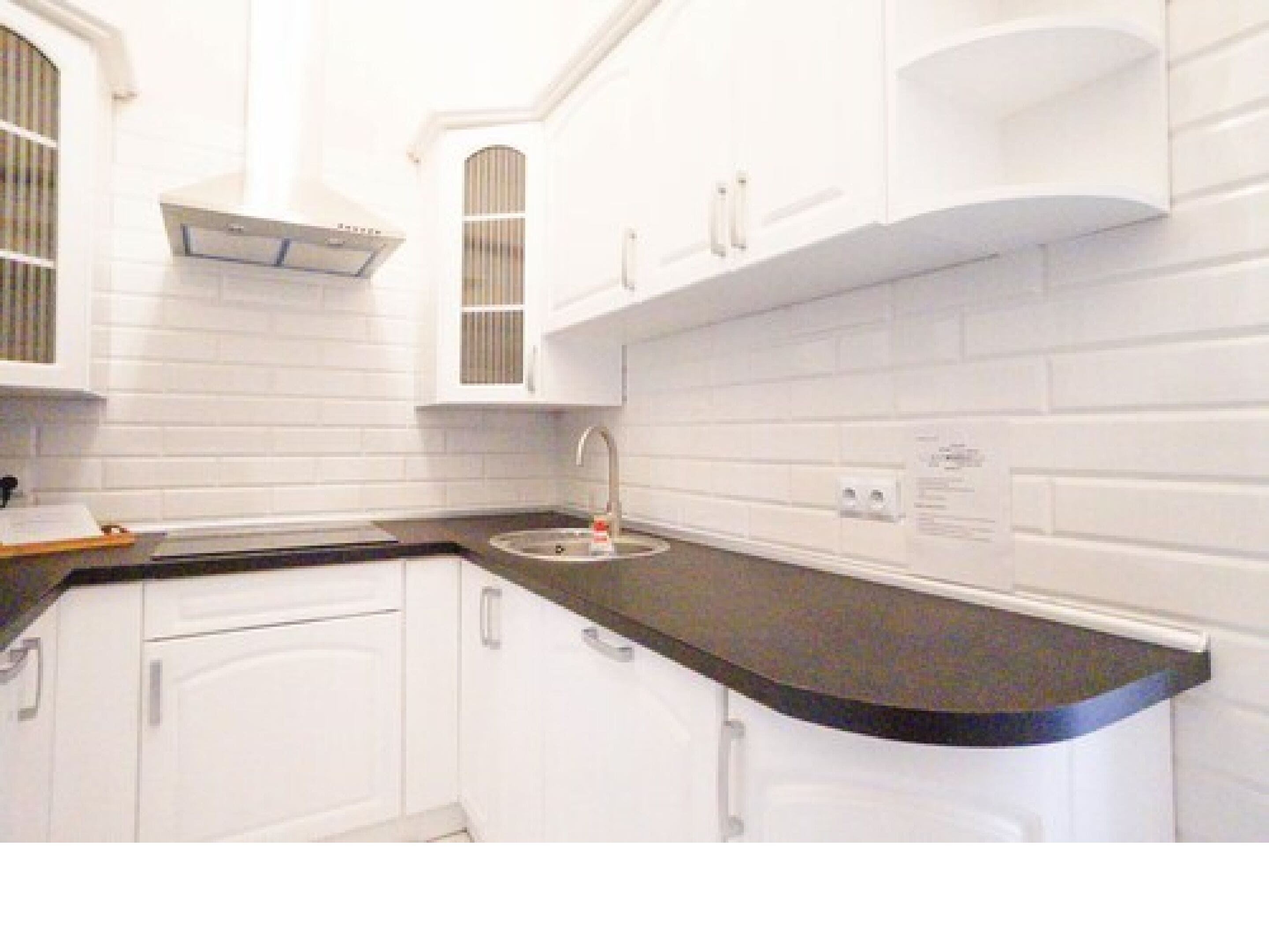 A modern kitchen with white cabinets, a black countertop, and a stainless steel sink.