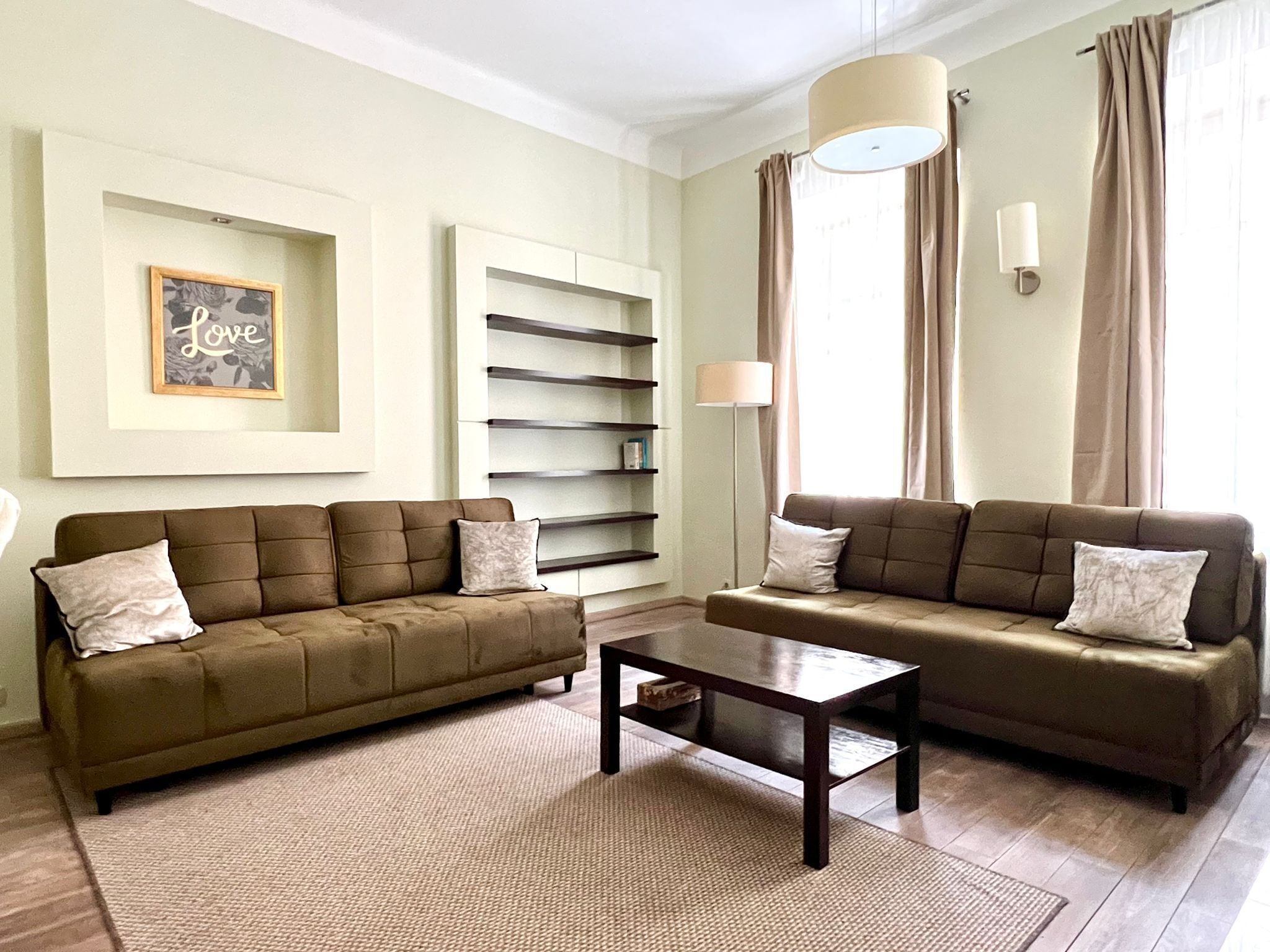 A living room with two sofas, a coffee table, a bookshelf, and a wall-mounted lamp.