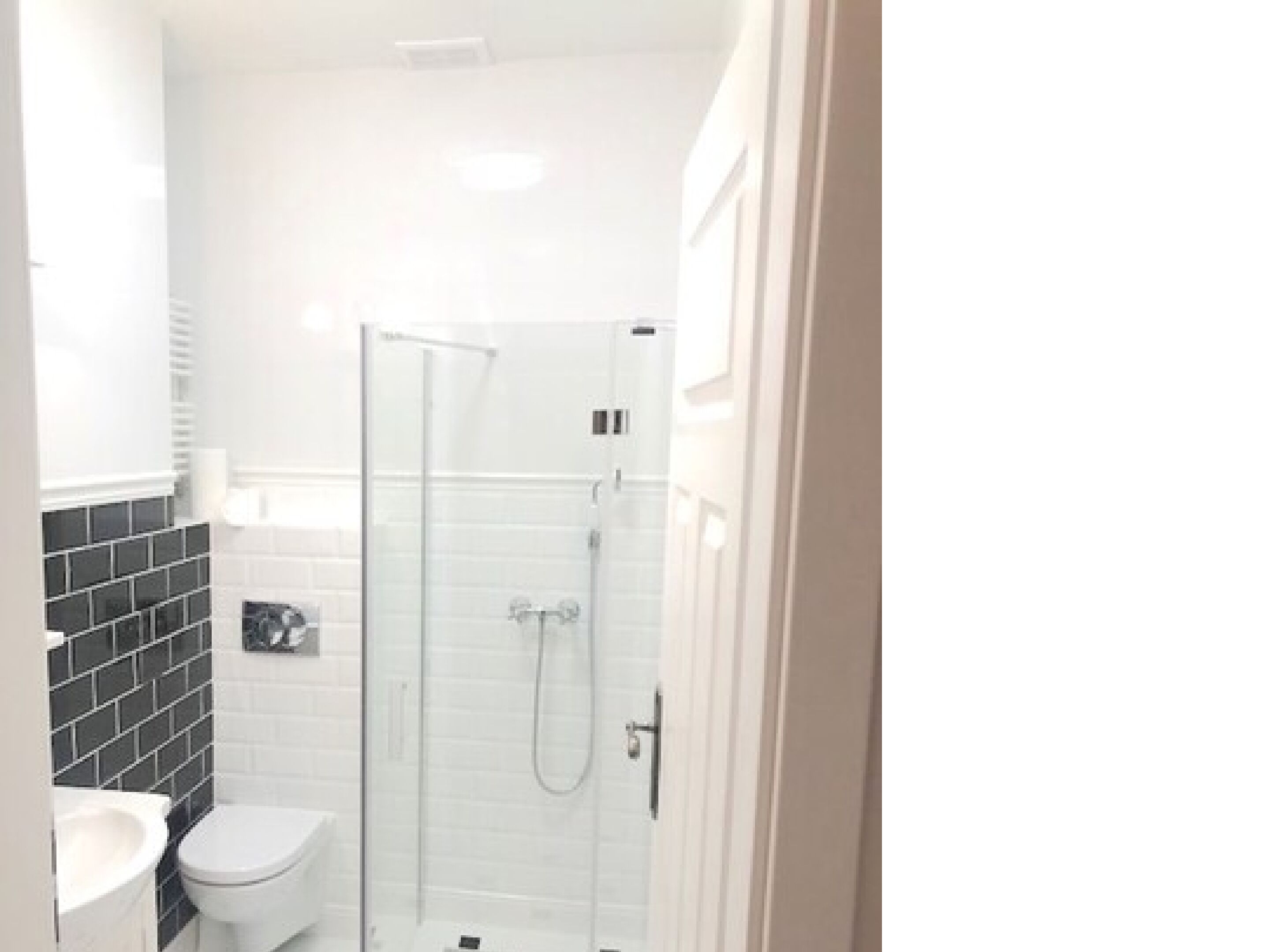 Ein kleines, weißes Badezimmer mit einer Duschkabine, einer Toilette und einem Waschbecken.