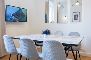 Ruokailutilassa on marmoripöytä, neljä harmaata tuolia, seinälle asennettu televisio ja koristeellinen kasvi.