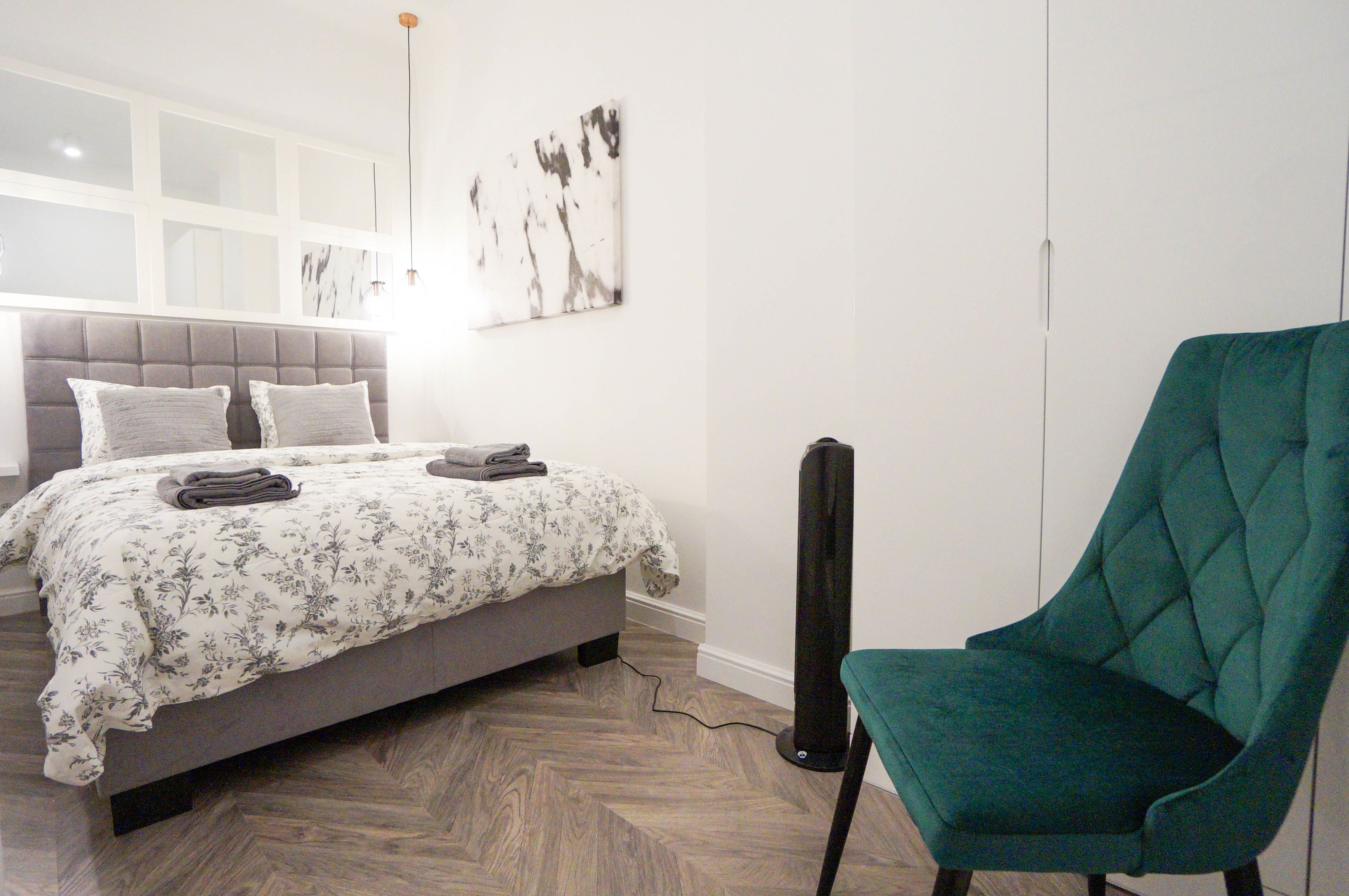 Un dormitorio con cama, una silla y una obra de arte colgada en la pared.