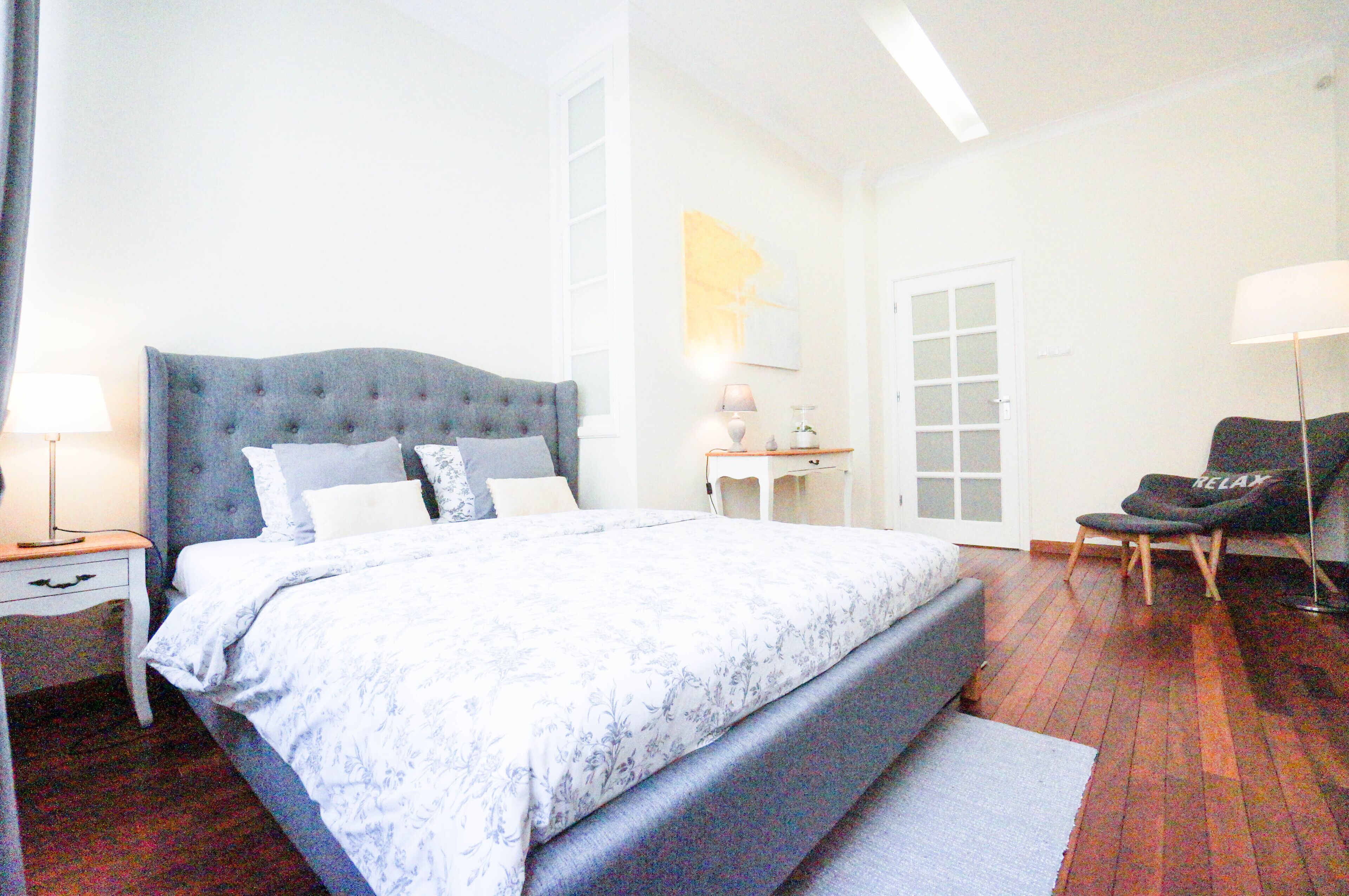 A bedroom with a large bed, a nightstand, a chair, and a door.
