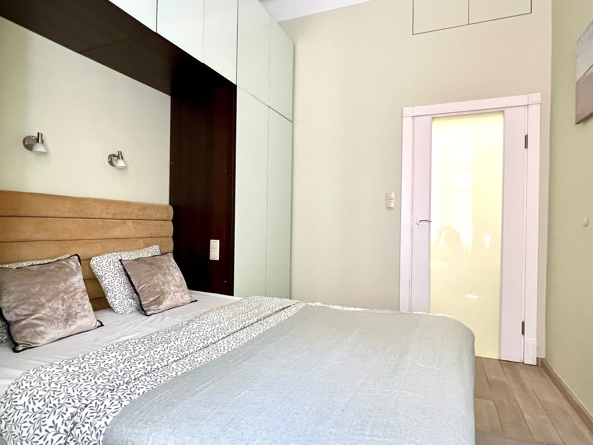A bedroom with a bed, two wall-mounted lights, a door, and a window.