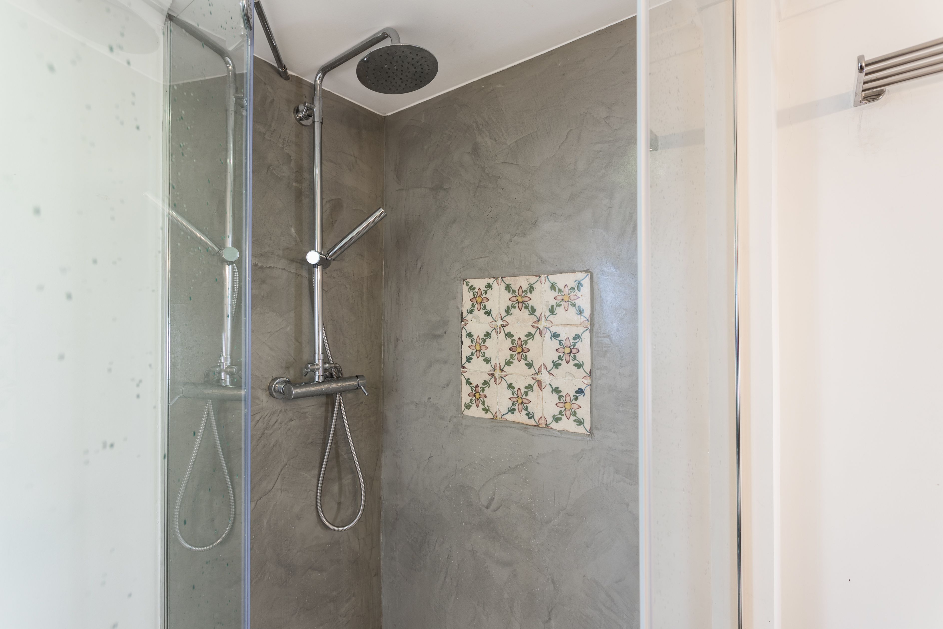 Une douche avec une porte en verre, un pommeau de douche à main et un panneau de commande fixé au mur.