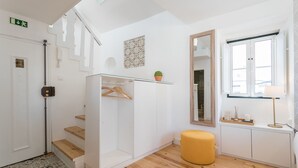 Een moderne hotelkamer met een wenteltrap, een glazen kast, een spiegel, een geel poef en een raam met uitzicht.