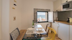 Een compacte keuken met een eettafel, stoelen en uitzicht op zee door een raam.