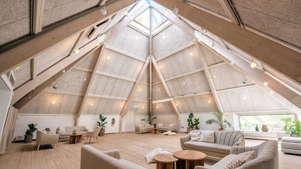 Amplia habitación estilo loft con techos altos, vigas de madera y ventanas grandes.