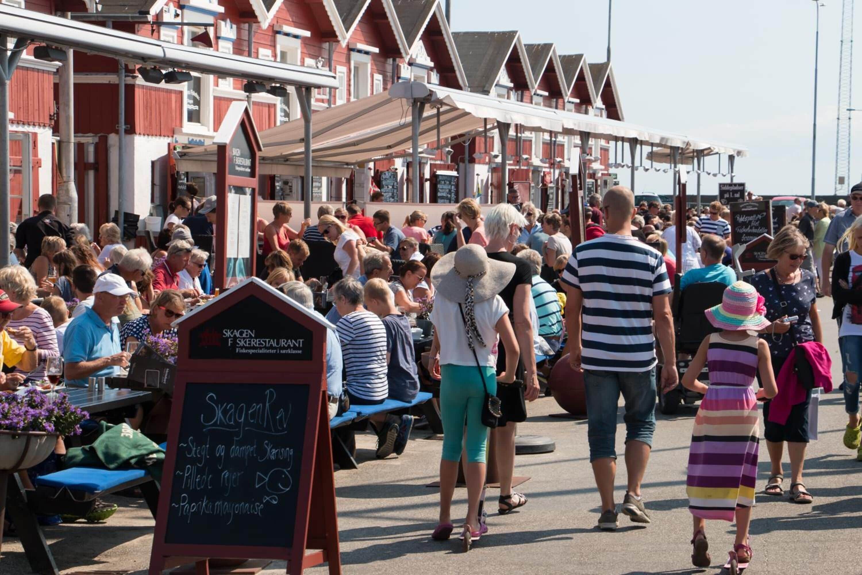 A crowded outdoor market with people walking and sitting at tables.