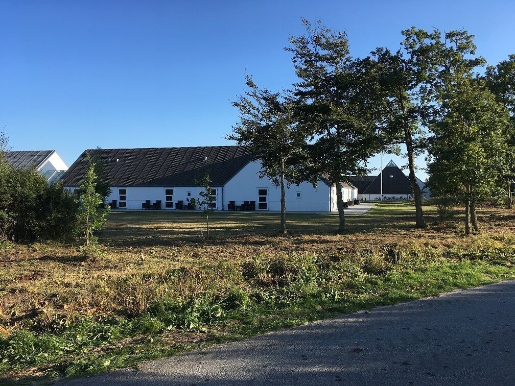 A white building with a sloped roof, surrounded by grass and trees.