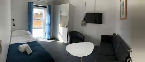 A hotel room with a bed, a sofa, a small table, a TV, and a window with curtains.