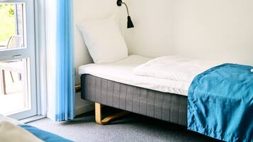 Un dormitorio con una cama, una ventana con cortinas, una lámpara de pared y un cuadro enmarcado.