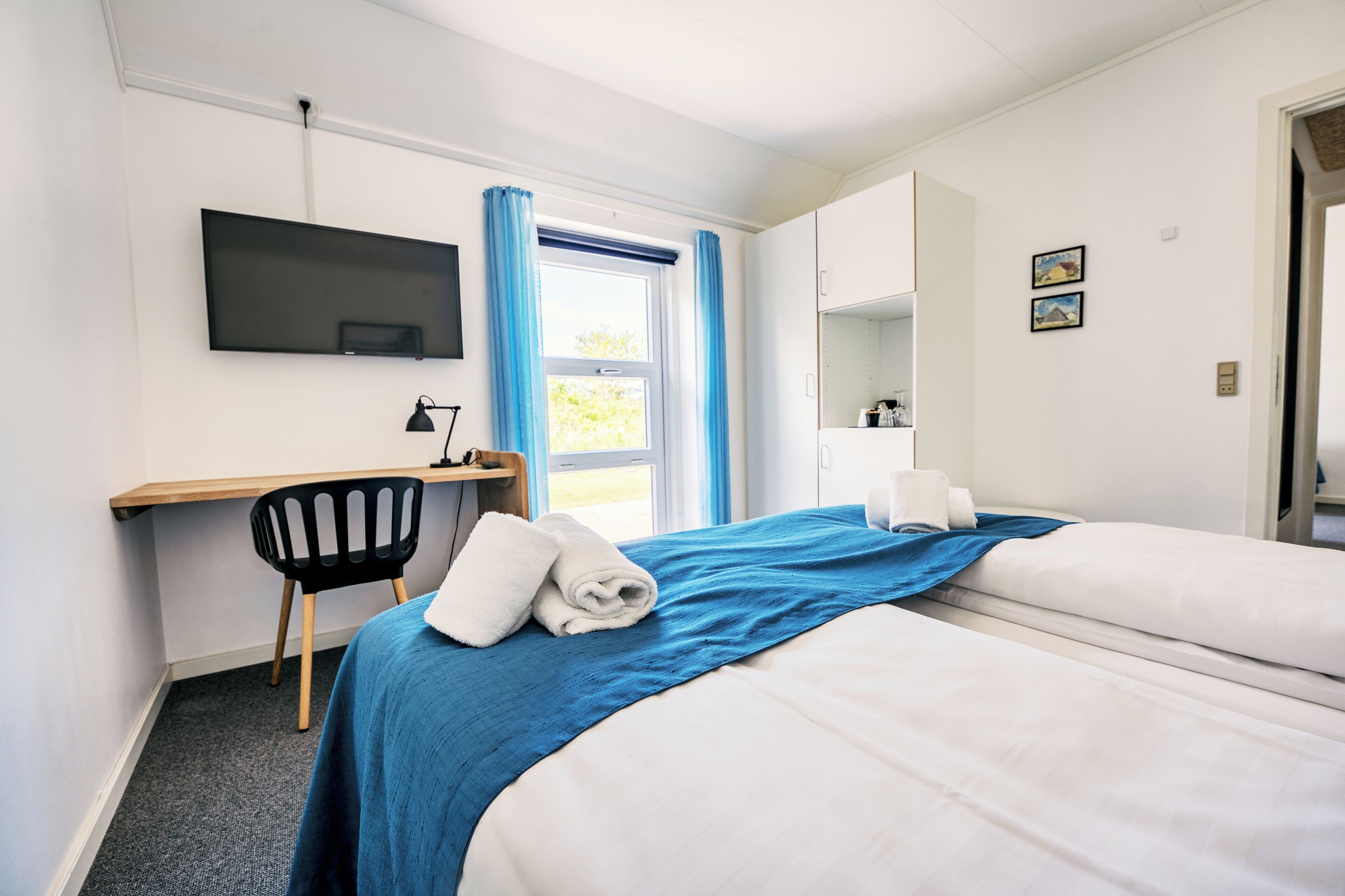A hotel room with two beds, a desk, a chair, a TV, and a window with curtains.