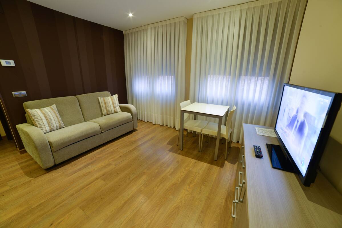 A modern living room with a sofa, a small table, a TV, and a remote control.